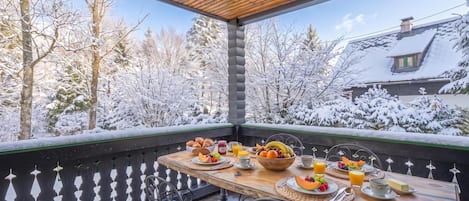 A wooden deck with a table set for breakfast, overlooking a snowy landscape.
