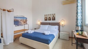 A hotel room with a bed, bedside tables, a nightstand, a window with curtains, and wall art. - Alcamo Pool House (Alcamo)