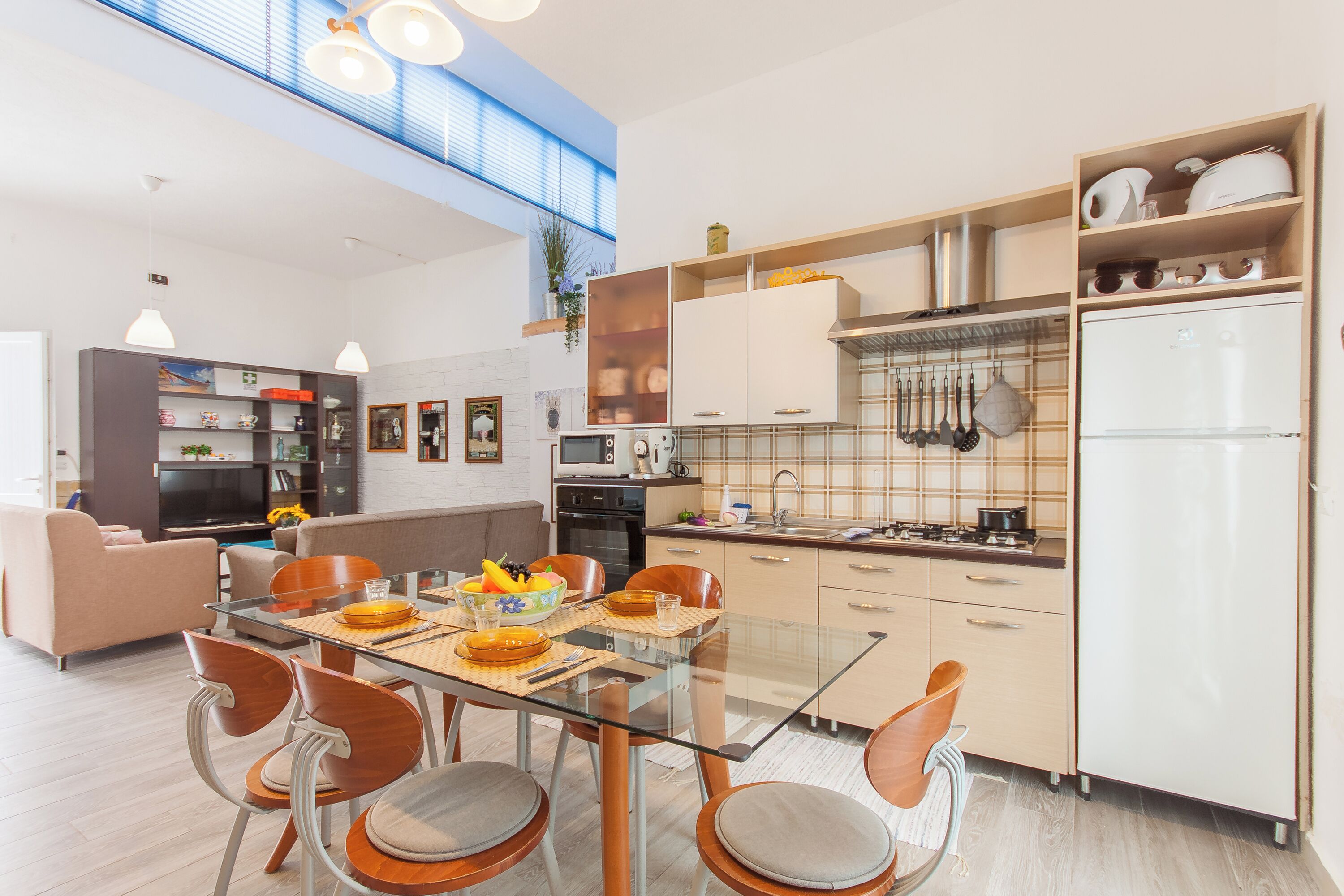 Una cocina moderna con comedor, que incluye una mesa de vidrio, sillas de madera y un horno empotrado.