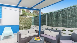 An outdoor patio area with wicker furniture, a table with fruit, and a view of a green fence. - Alcamo Pool House (Alcamo)