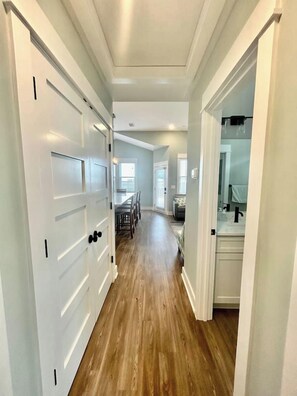 A hallway with wooden flooring, white doors, and a view into a dining area with a table and chairs. - Relax on Island Time, 2 Bed Single Level Condo (Corolla)