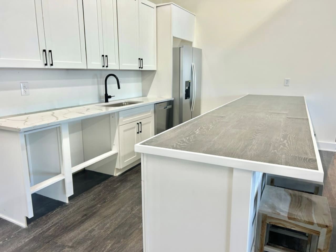 Una cocina con armarios blancos, un refrigerador de acero inoxidable y una encimera de madera.