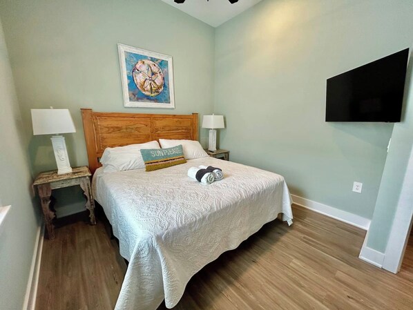 A bedroom with a bed, two bedside tables, a wall-mounted TV, and a painting.