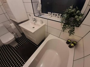 A bathroom with a white sink, toilet, and bathtub. There is a mirror above the sink and a plant on the wall.