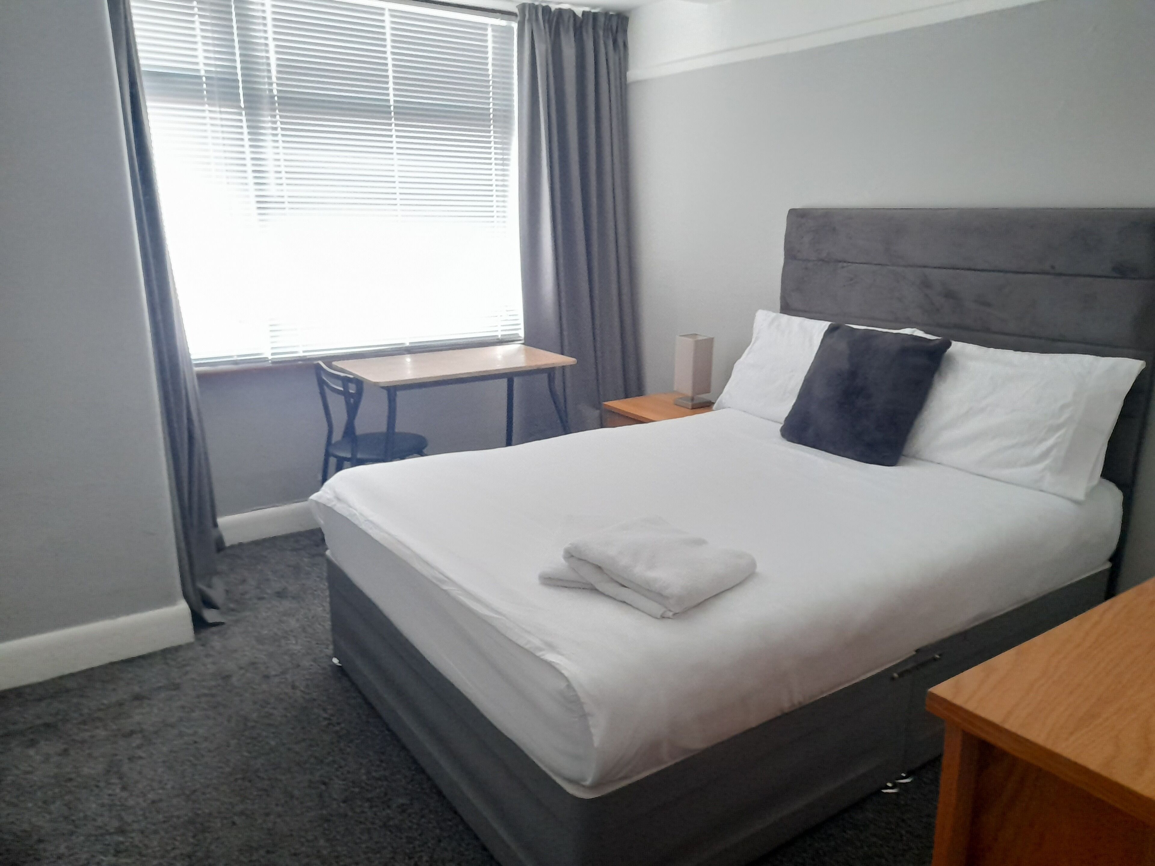 Habitación de hotel con una cama grande, una mesita pequeña, una silla y una ventana con cortinas.