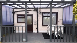 Un espace extérieur abrité, doté d’une terrasse en bois, d’une porte et de deux fenêtres.