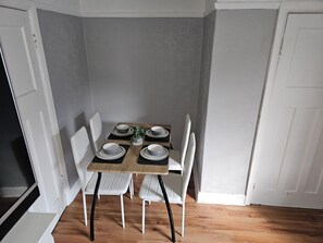 A dining area with a wooden table set for four, white chairs, and a potted plant.