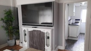 Un salon doté d’un téléviseur à écran plat fixé au-dessus d’une cheminée, d’une plante en pot et d’une vue sur la cuisine.