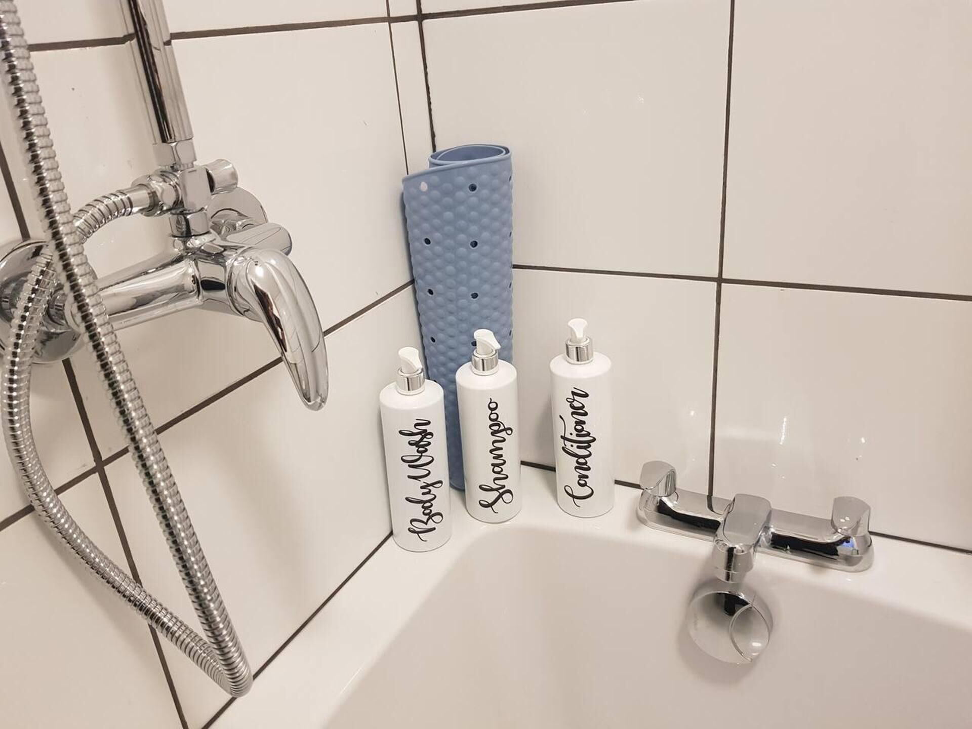 Ein Badezimmer mit Dusche, Badewanne und drei Flaschen Shampoo, Conditioner und Duschgel.
