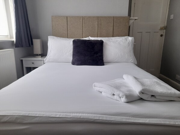 A neatly made bed with white linens and a folded white towel.