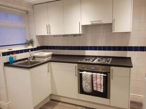 A modern kitchen with white cabinets, a black countertop, a stainless steel sink, and a built-in oven.