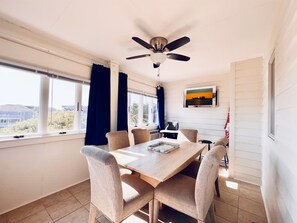 Enjoy meals in this dining area with a wooden table and six chairs, surrounded by large windows and a beautiful painting.