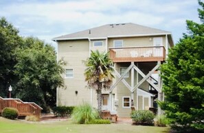 A two-story building with a balcony on the second floor, surrounded by greenery. - Private Pool, Tiki Bar, Beach & Sound Access (Kitty Hawk)