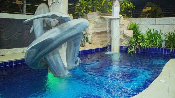 An indoor swimming pool with a large sculpture, a waterfall feature, and tiled walls. - HG PALACE LODGE (Accra)