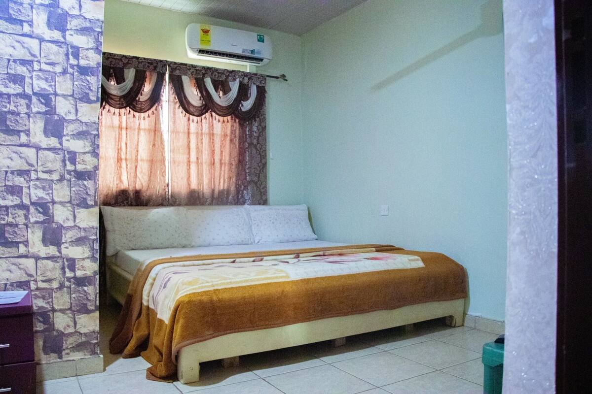 Une chambre à coucher avec un lit, un mur en pierre, un climatiseur et un rideau.
