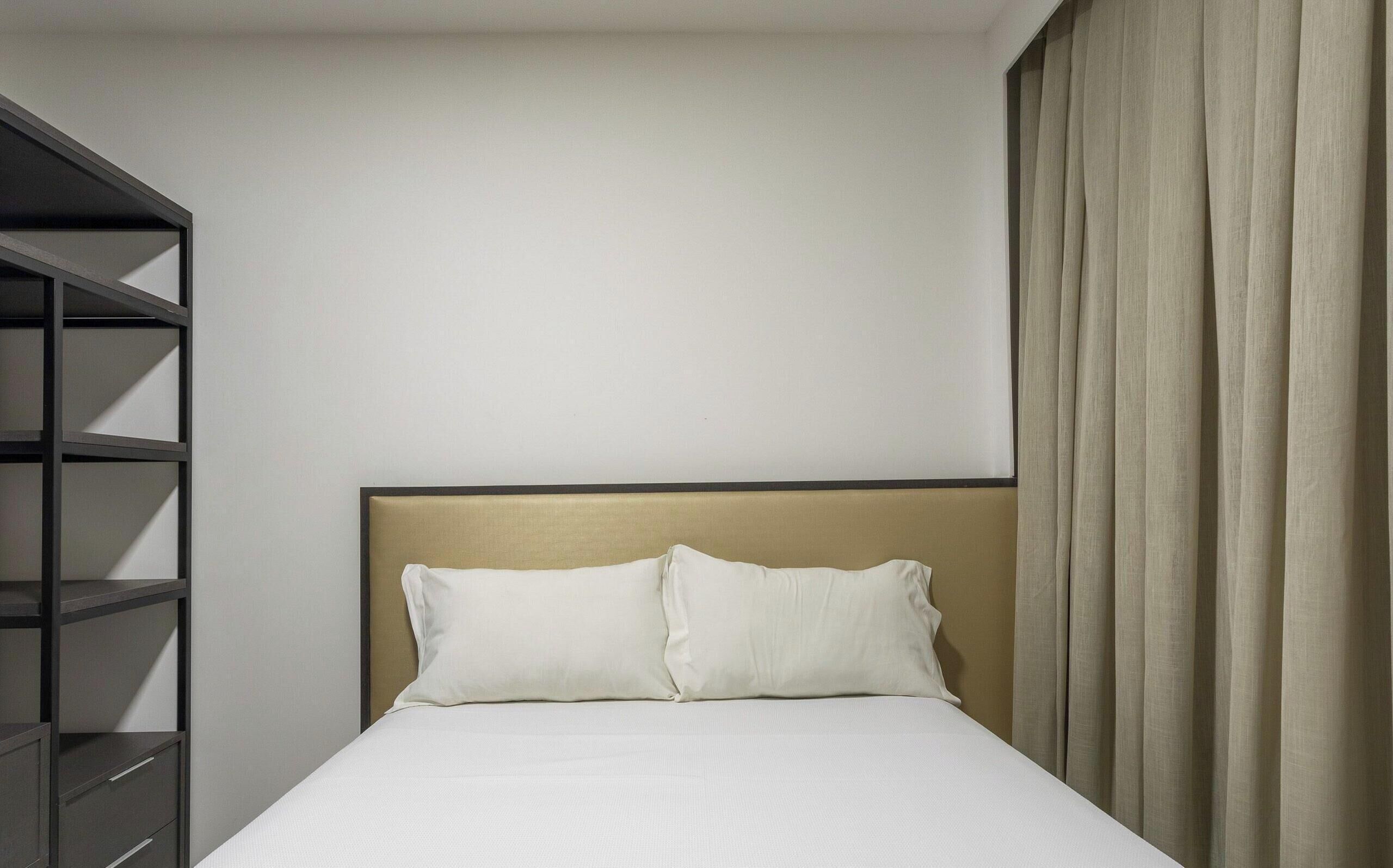 Habitación de hotel con cama, cabecera, armario y cortina.