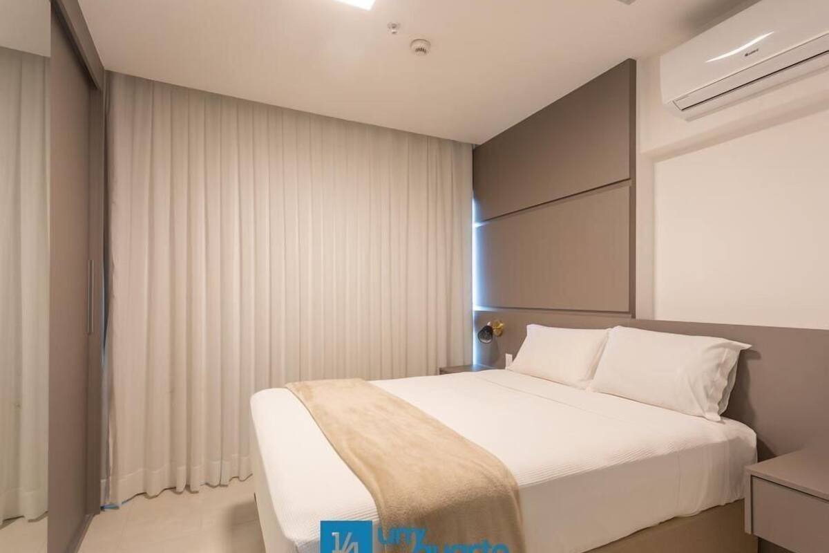 A modern hotel room with a large bed, a bedside table, a nightstand, and an air conditioning unit on the wall.