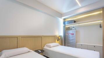 A hotel room with two single beds, a bedside table, a small round table, and a wardrobe with a mirror.