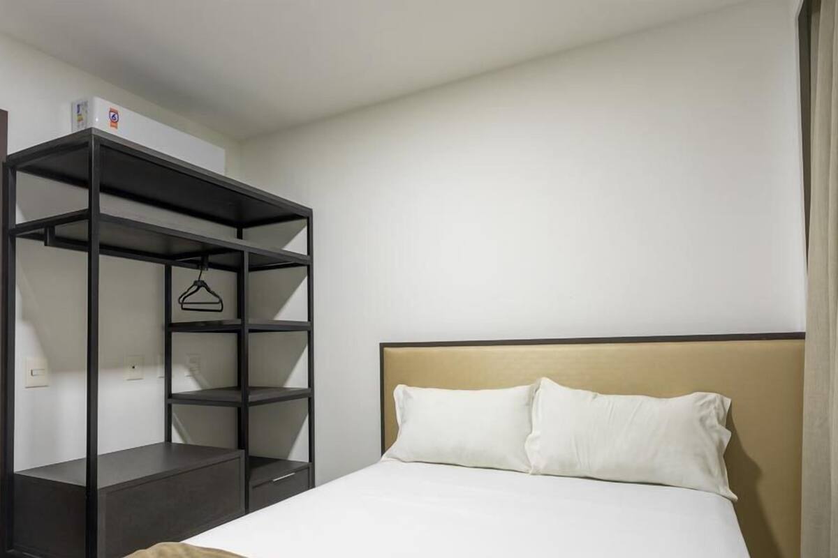 A hotel room with a bed, a black shelving unit, and a white headboard.