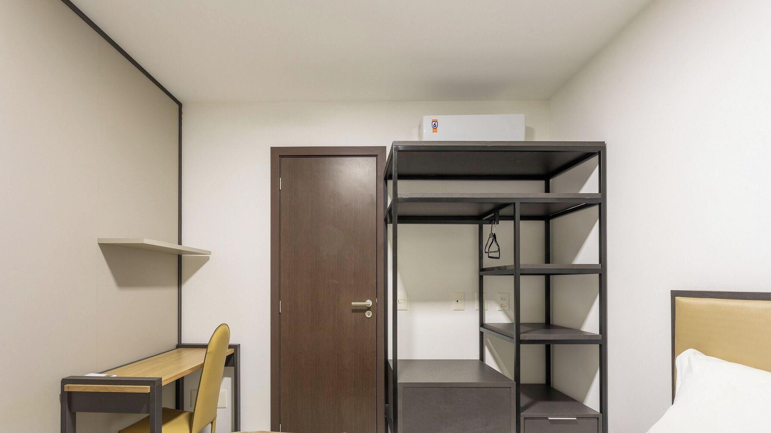 Una habitación compacta con cama, escritorio y armario empotrado con estantes.