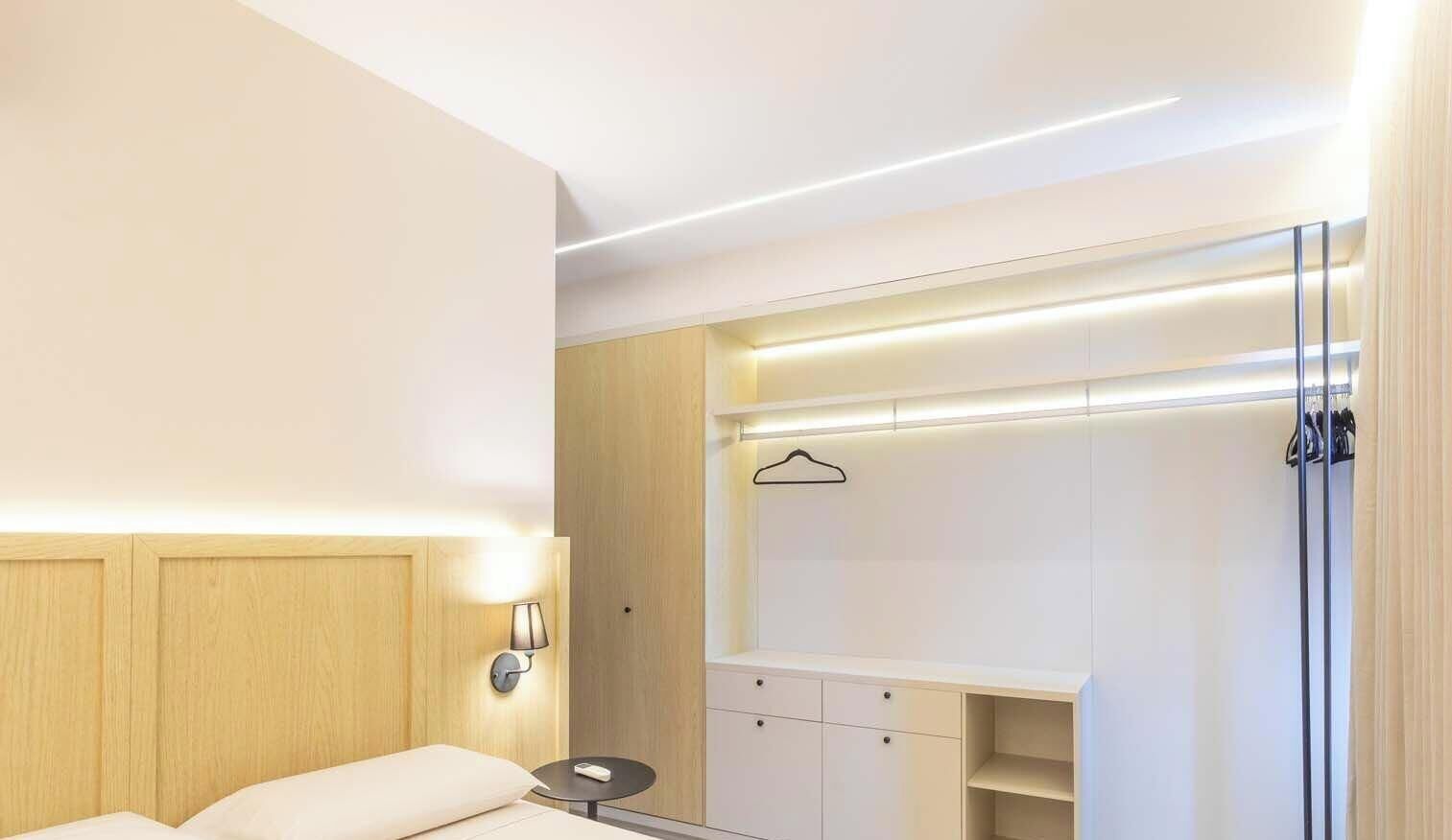 Ein Hotelzimmer mit Bett, Nachttisch, Lampe, Kleiderschrank und einer Garderobe.