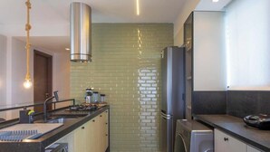 A modern kitchen with a stainless steel range hood, a built-in oven, a refrigerator, and a washing machine. - Complexo Heron Marinho Flats (Campina Grande)