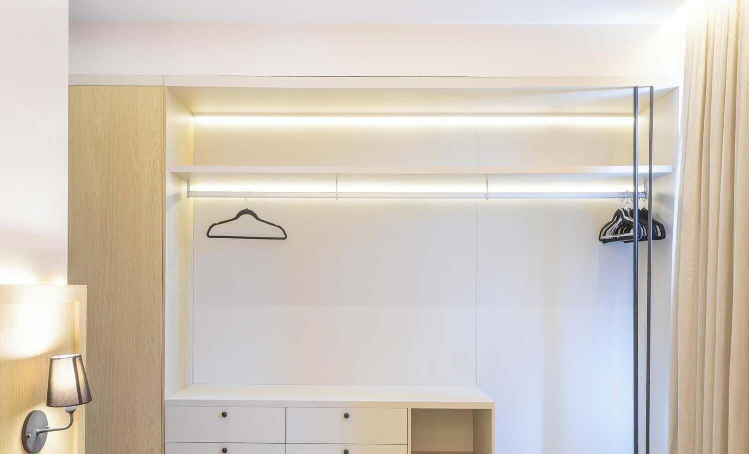 A hotel room with a walk-in closet, a hanging garment rack, and a bedside table.