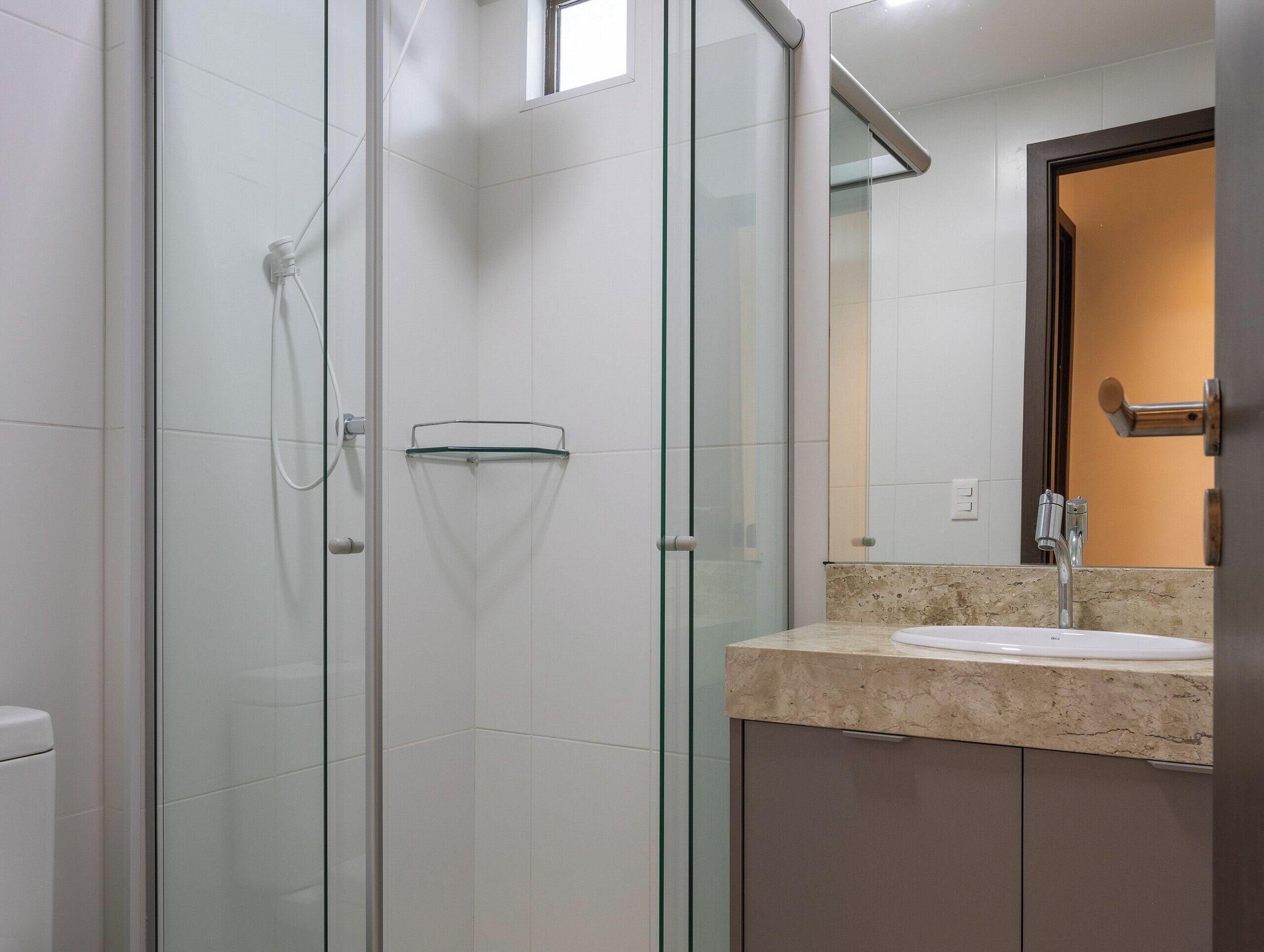A modern bathroom with a glass shower enclosure, a glass door, a sink with a marble countertop, and a mirror above the sink.