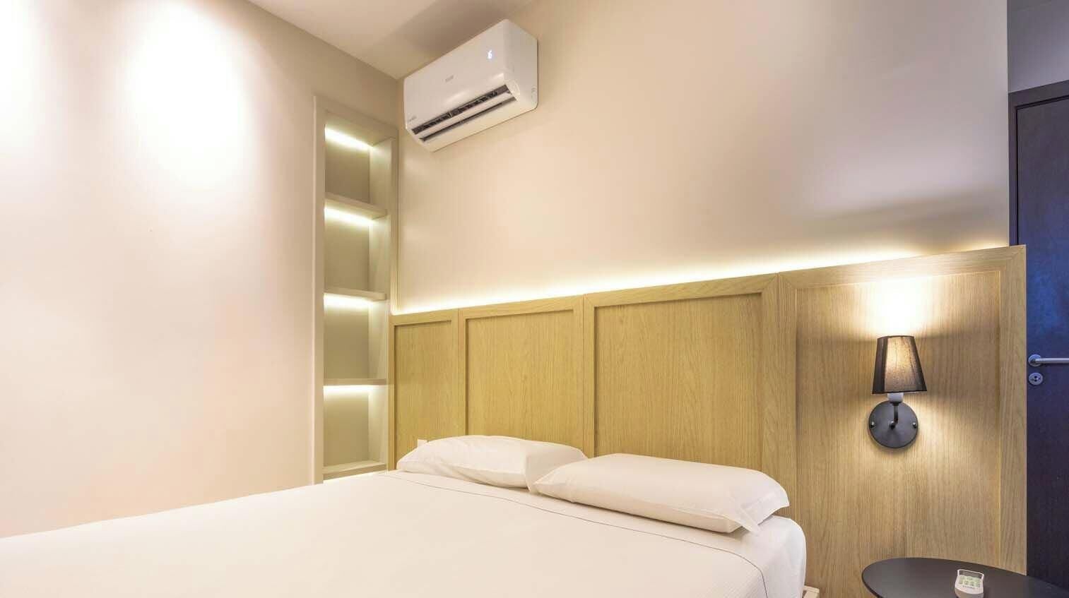 Una habitación de hotel con cama, unidad de aire acondicionado, mesita de noche y lámpara de pared.