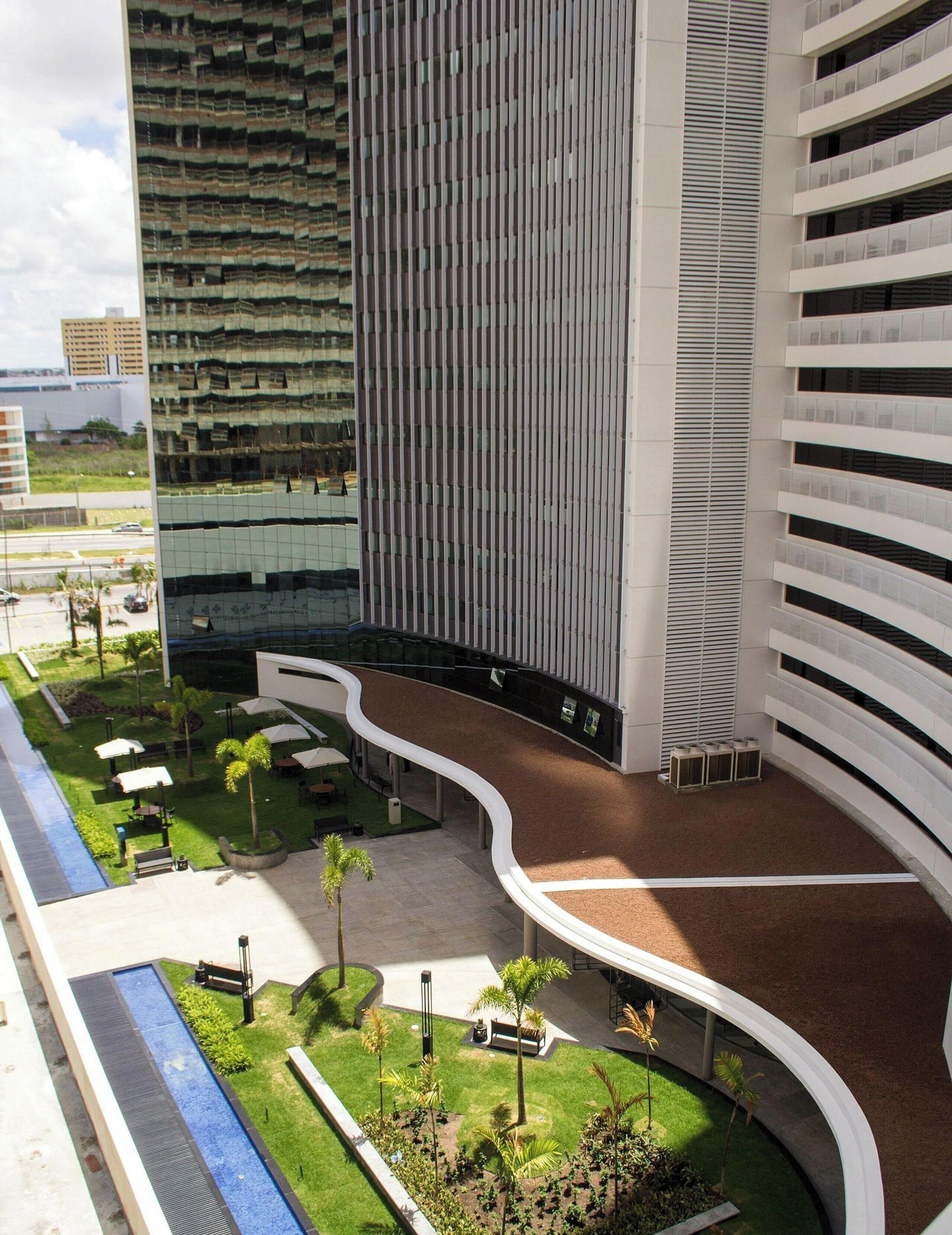 A modern building with a curved pathway, outdoor seating, and greenery.