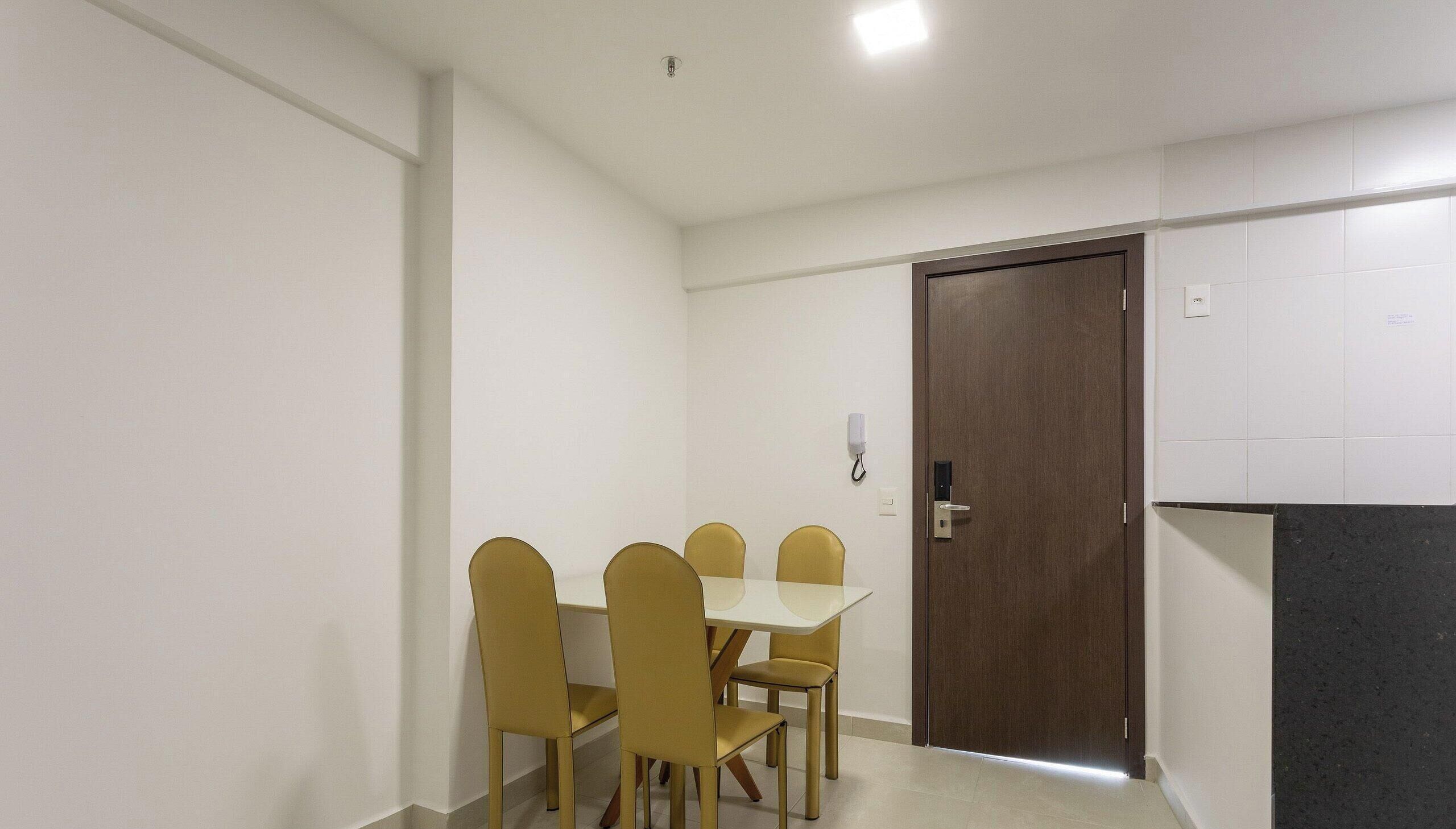 A small, well-lit room with a wooden door, a white table, and four chairs.