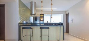 A modern kitchen with a central island, bar stools, a stainless steel range hood, and a hanging light fixture. - Complexo Heron Marinho Flats (Campina Grande)