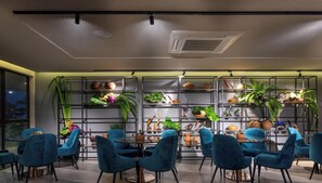 Un espace repas moderne avec des chaises bleues, une table ronde et des étagères ornées de plantes et de poteries.