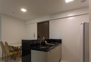 Cocina moderna con encimera negra, pileta de acero inoxidable y horno empotrado. A la izquierda, un comedor con mesa y sillas.