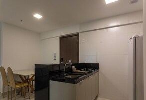 Cocina moderna con encimera negra, pileta de acero inoxidable y horno empotrado. A la izquierda, un comedor con mesa y sillas.