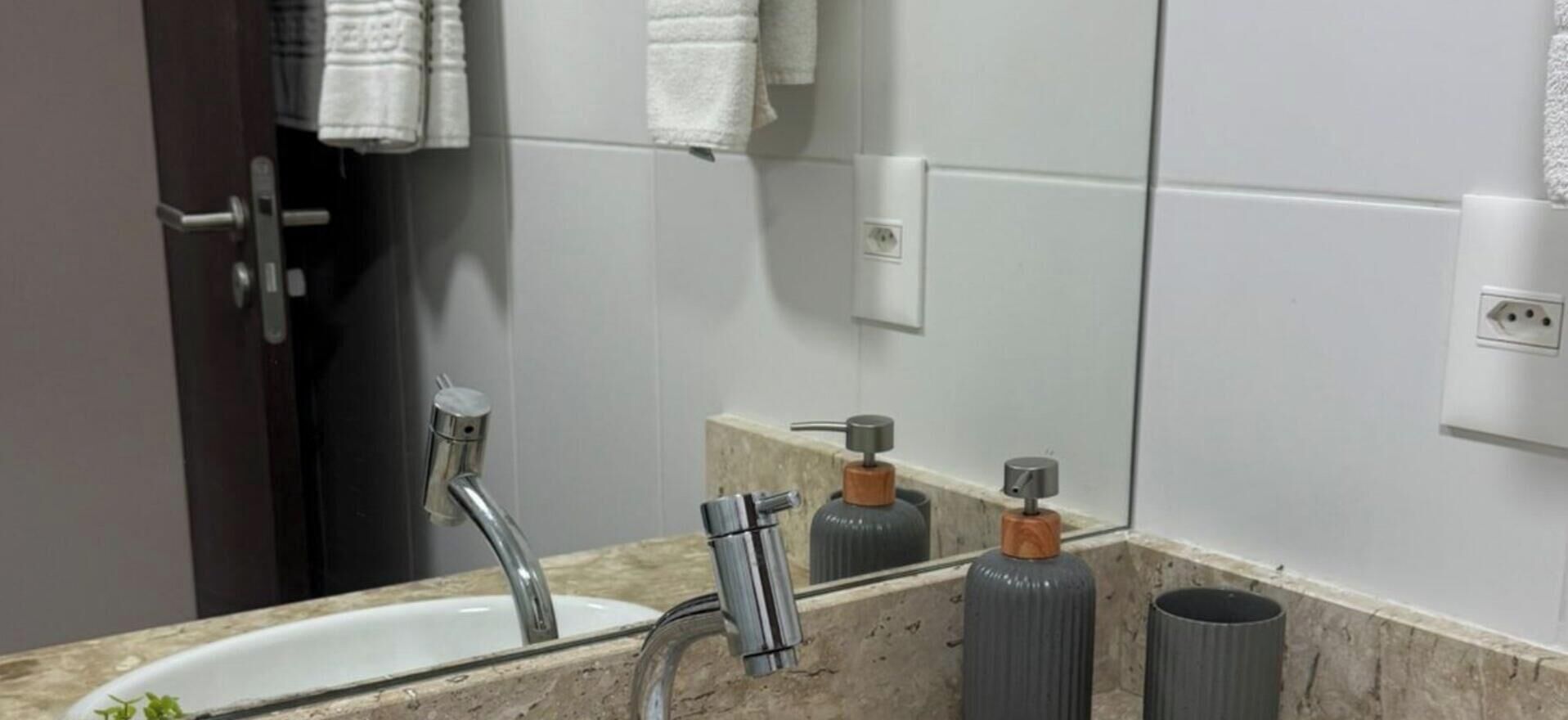 A bathroom with a sink, a mirror, and two soap dispensers.