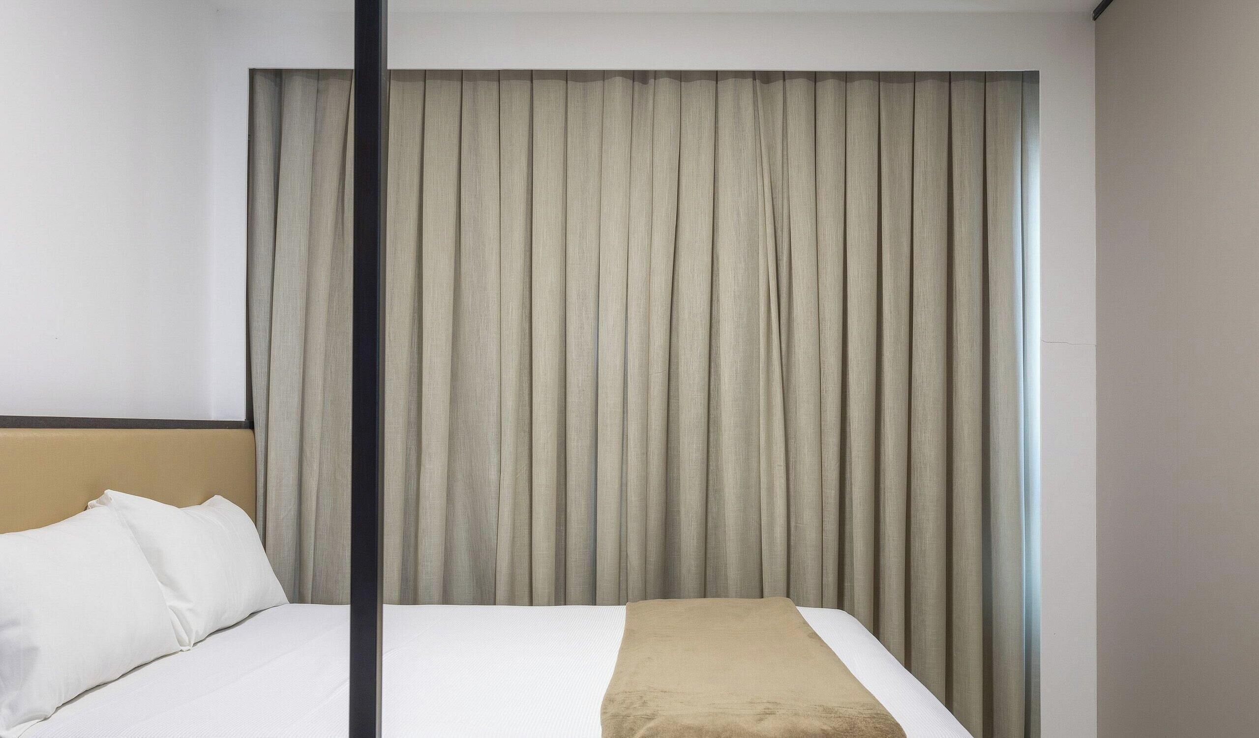 A hotel room with a bed, a headboard, and a large window with curtains.