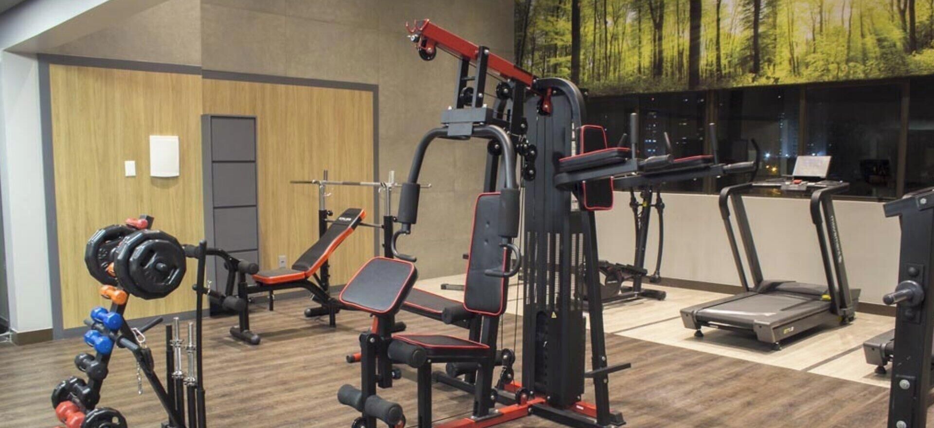 Un gimnasio con varios equipos de ejercicio, incluyendo una jaula de sentadillas, una banca de press y cintas de correr.