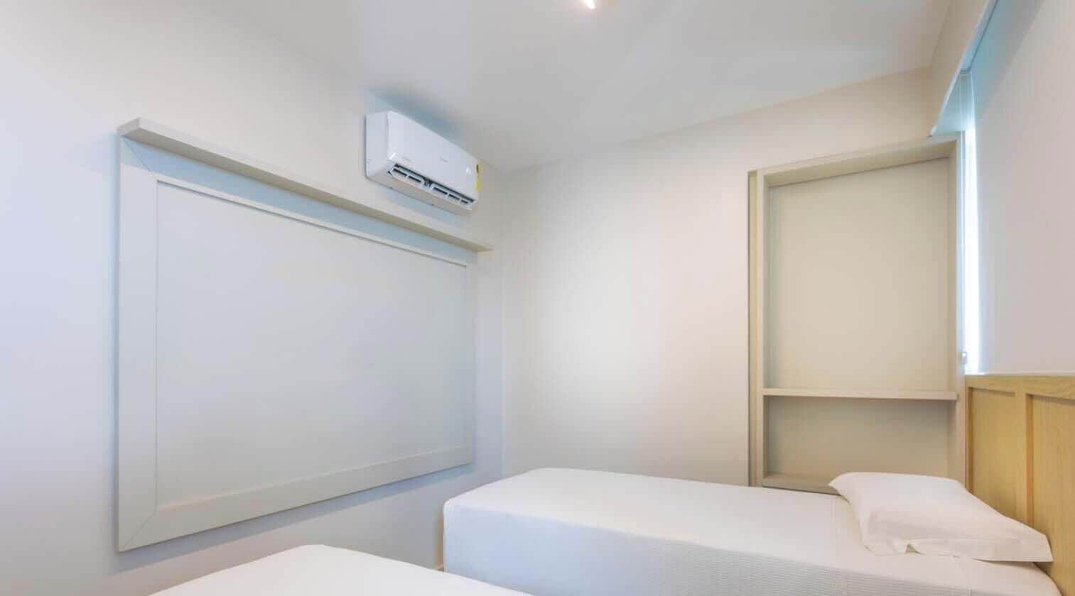 Habitación de hotel con dos camas individuales, aire acondicionado de pared y estante empotrado.