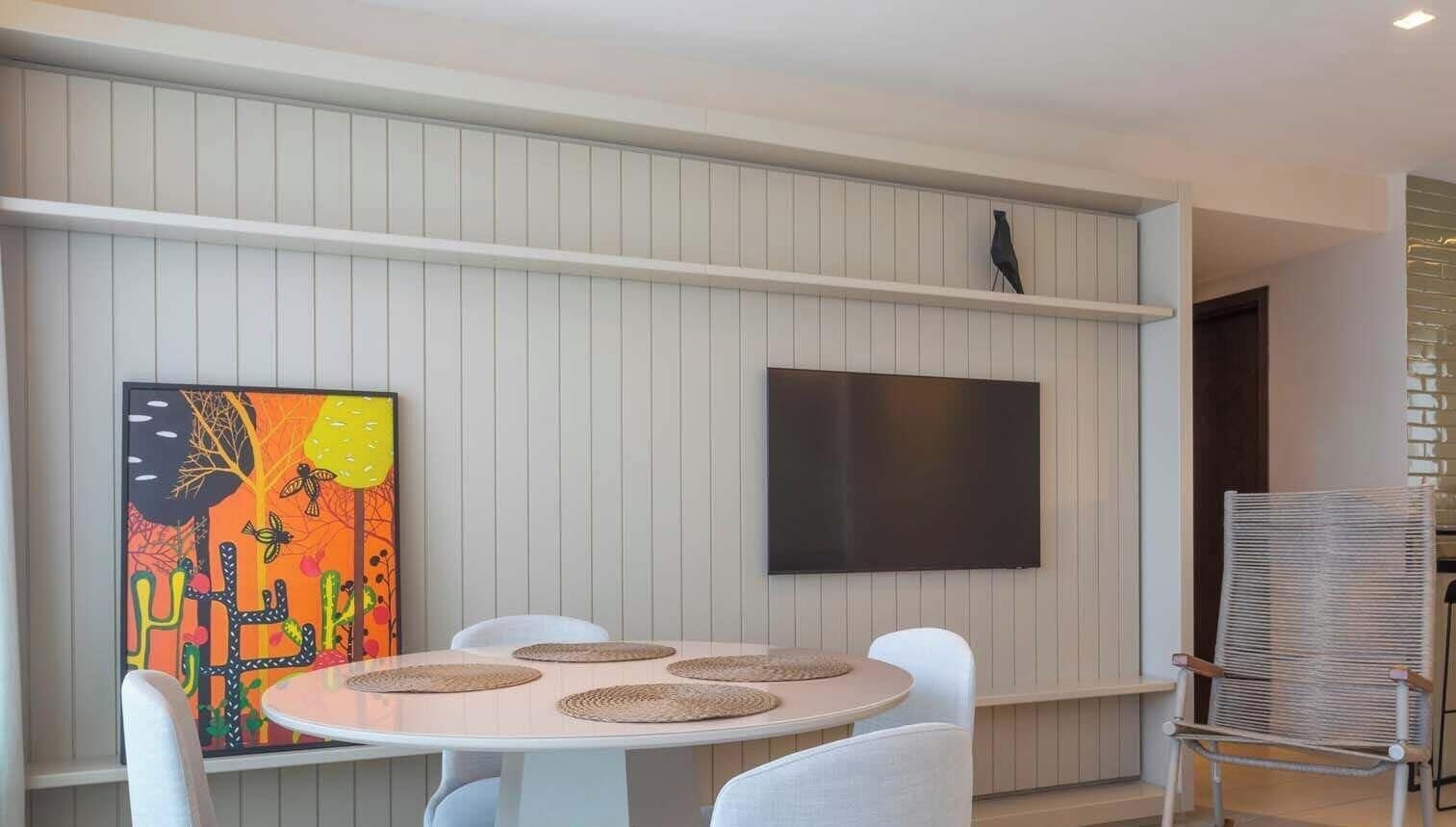 Un comedor moderno con una mesa redonda, sillas blancas, un televisor de pantalla plana en la pared y un cuadro abstracto colorido a la izquierda.