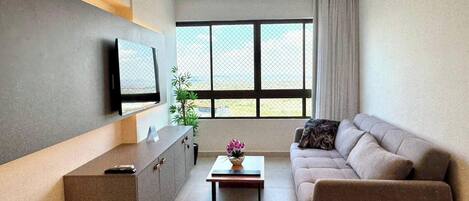 Ein stilvolles Wohnzimmer mit einer Couch, einem Couchtisch, einem an der Wand befestigten Fernseher und einem großen Fenster mit Ausblick.