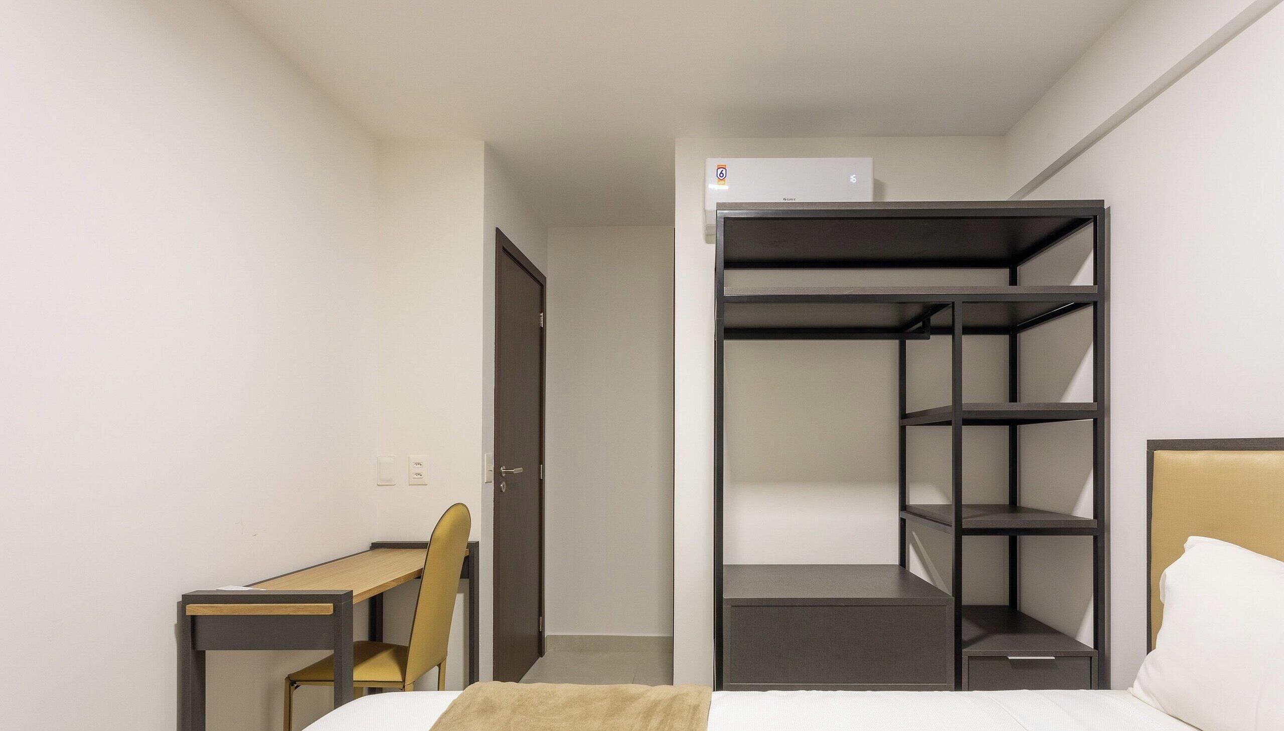 A compact hotel room with a bed, a desk, a chair, and a built-in wardrobe with shelves.