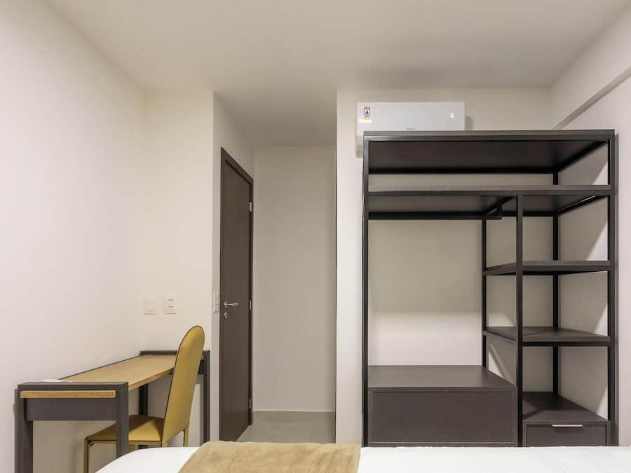 Habitación de hotel pequeña con cama, escritorio, una silla y armario empotrado con estantes.