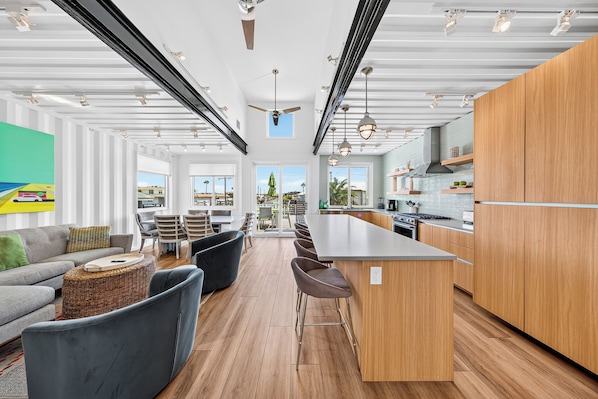 A modern kitchen with a central island, bar stools, and a dining area with a sofa and chairs.