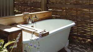 A freestanding bathtub with a wooden vanity and sink, surrounded by a wooden fence and plants. - Hurdlemakers Hut (Dorchester)