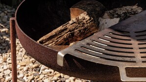 A metal grill with a slotted grate, a wooden log, and a metal handle. - Hurdlemakers Hut (Dorchester)