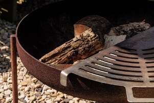 Una parrilla metálica con rejilla ranurada, un tronco de madera y un asa metálica.