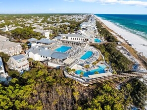 Vista aérea de un complejo turístico frente al mar, con varias piscinas y abundante vegetación.