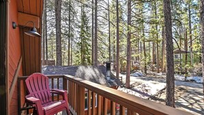 Eine Holzterrasse mit einem roten Adirondack-Sessel, umgeben von hohen Kiefern.