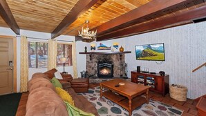 Ein gemütliches Wohnzimmer mit Kamin, Holzbalken, einer Couch und einem Fernseher.